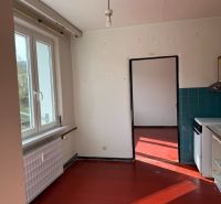 A kitchen of a 2-room apartment with a red floor and a window, light walls, dark tiles.