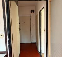 A hallway in a 2-room apartment with light paint and red linoleum flooring.