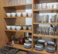 Kitchen cabinet with glasses, bowls, and cutlery on wooden shelves.