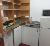 Kitchen corner in offices with appliances, wooden shelves, and red flooring.