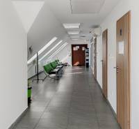 A hallway in offices with white walls, green chairs, and tiles.