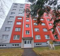An apartment building in Poprad with a red facade, in front of which there is a sidewalk and trees.