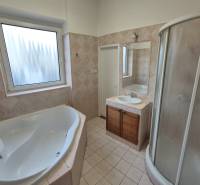 A bathroom with a bathtub and shower in a 3-room apartment, tiles with a subtle pattern.