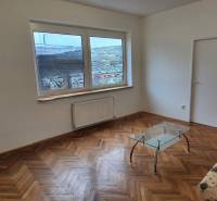 Living room with a sofa, glass table, and wood-patterned flooring in a three-room apartment.