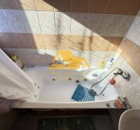 Bathroom with a bathtub in a family house, tiled with beige and white tiles.