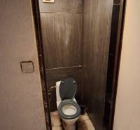 A toilet with ceramic tiles in a 3-room apartment, dark tiling and ventilation.
