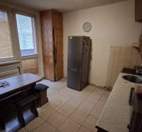 A kitchen in a 3-room apartment with tiles and simple furniture, a refrigerator, and a dining table.