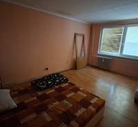 A room with a wooden floor design, a simple bed, and a dresser in a three-room apartment.