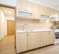 A kitchen in a 2-room apartment with a wooden decor floor and light furniture.