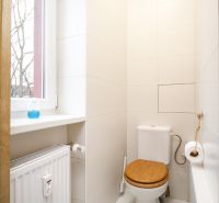 Bathroom in a 2-room apartment with a toilet, radiator, and window. White tiles.
