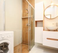 Bathroom in a 2-room apartment with a washing machine, shower cabin, and sink on a wooden decor.