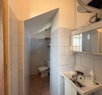 A bathroom in a family house with a sink and a toilet, tiled with light tiles.