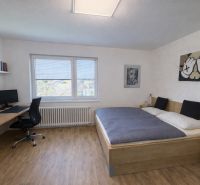 A bedroom in a family house with a bed, a desk, and a wooden decor floor.