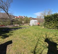 A garden at a family house in Koválov with a lawn, greenhouse, and trees.