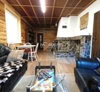 The interior of a cabin with a wooden decor floor, a stone fireplace, and a leather sofa.