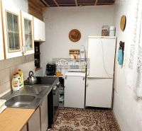 A kitchen in a cottage with simple furnishings, a carpet, and a white refrigerator.