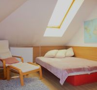 Attic room in a holiday apartment with a bed, chair, and wooden decor flooring.