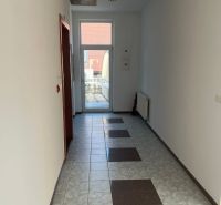 The image shows a bright corridor with a tiled floor leading to an office.