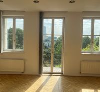 An empty room with parquet flooring, large windows, and a view of Štefánikova Street, suitable for offices.
