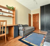 Room in a 3-room apartment with a shelf, gray sofa, and a desk.