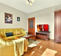 Living room with wood-patterned flooring, yellow sofa, and decorative paintings in a three-room apartment.