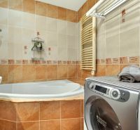 A bathroom in a 3-room apartment with a corner bathtub, washing machine, and clothes dryer.