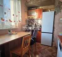 A kitchen in a 3-room apartment with a wooden table, refrigerator, and decorative curtains.