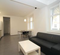 Living room in a two-room apartment with seating, kitchenette, and table on tiles.