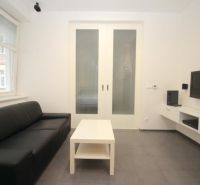 Living room in a two-room apartment with a dark sofa and a TV on the wall.
