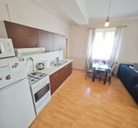 A kitchen in a 2-room apartment with a wooden decor floor and a dining area.