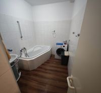 A bathroom in a 2-room apartment with a corner bathtub and a floor with a wooden decor.