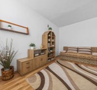Living room with a sofa, wooden furniture, and a floor with a wood pattern in a three-room apartment.
