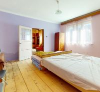 Bedroom in a family house with a bed, wood-patterned flooring, and light pink walls.