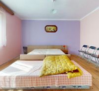 A bedroom in a family house with a yellow blanket, folding chairs, and a wooden decor floor.