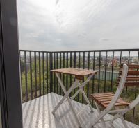 A balcony with wooden chairs and a table in a 2-room apartment with a view of the countryside.