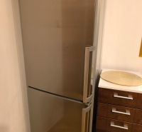 A stainless steel refrigerator in the corner of the kitchen of a three-room apartment with an adjacent wooden sideboard.