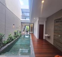 Villa with a pool, wooden decor flooring, plants, and a stone wall.