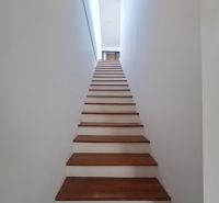 The staircase of the villa with a wooden decor floor and white walls.