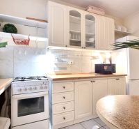 The kitchen in a studio apartment with white cabinets, a stove, and decorations on the shelves.