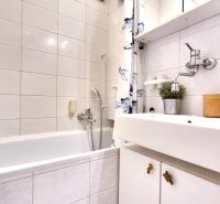 A bathroom in a studio apartment with a bathtub, a sink, and white tiles.