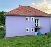 A family house in Kosihovce with a purple facade and a red roof on a grassy plot.