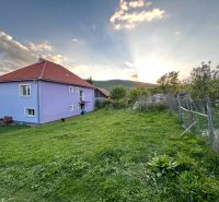 A family house in Kosihovce surrounded by a garden, with mountains and a setting sun in the background.