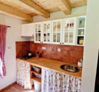 A kitchen in a cottage with white cabinets, ceramic tiles, and a wooden ceiling.