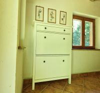 White cabinet with decorations, next to a wooden window, floor tiles behind the cottage.