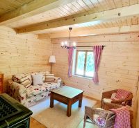 A wooden interior of a cabin with a stove, a sofa, and rattan chairs.