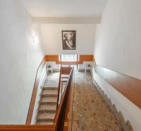 A staircase in a cottage with a portrait on the white wall, stone steps, wooden railing.