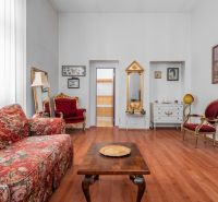Interior of a cottage with a floral sofa, decorative chairs, and a wooden-patterned floor.