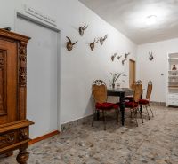 The interior of the cabin with a stone floor, hunting trophies, and a carved wooden cabinet.