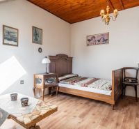 The interior of a cabin with wooden floor decor, a simple bed, and an antique chair.
