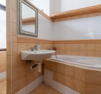 A bathroom in a cabin with a bathtub, sink, and window. Tiles in soft tones.